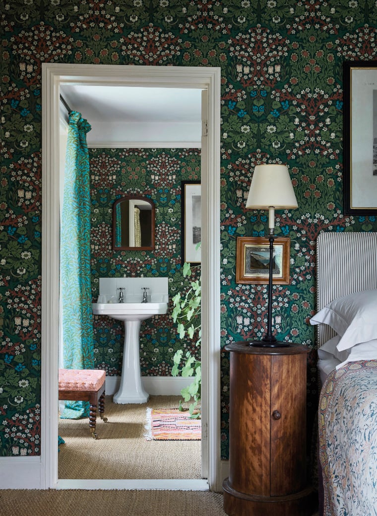 Blick von einem Schlafzimmer in ein Badezimmer. Die Wand ist mit der Tapete Blackthorn von Morris & Co tapeziert.